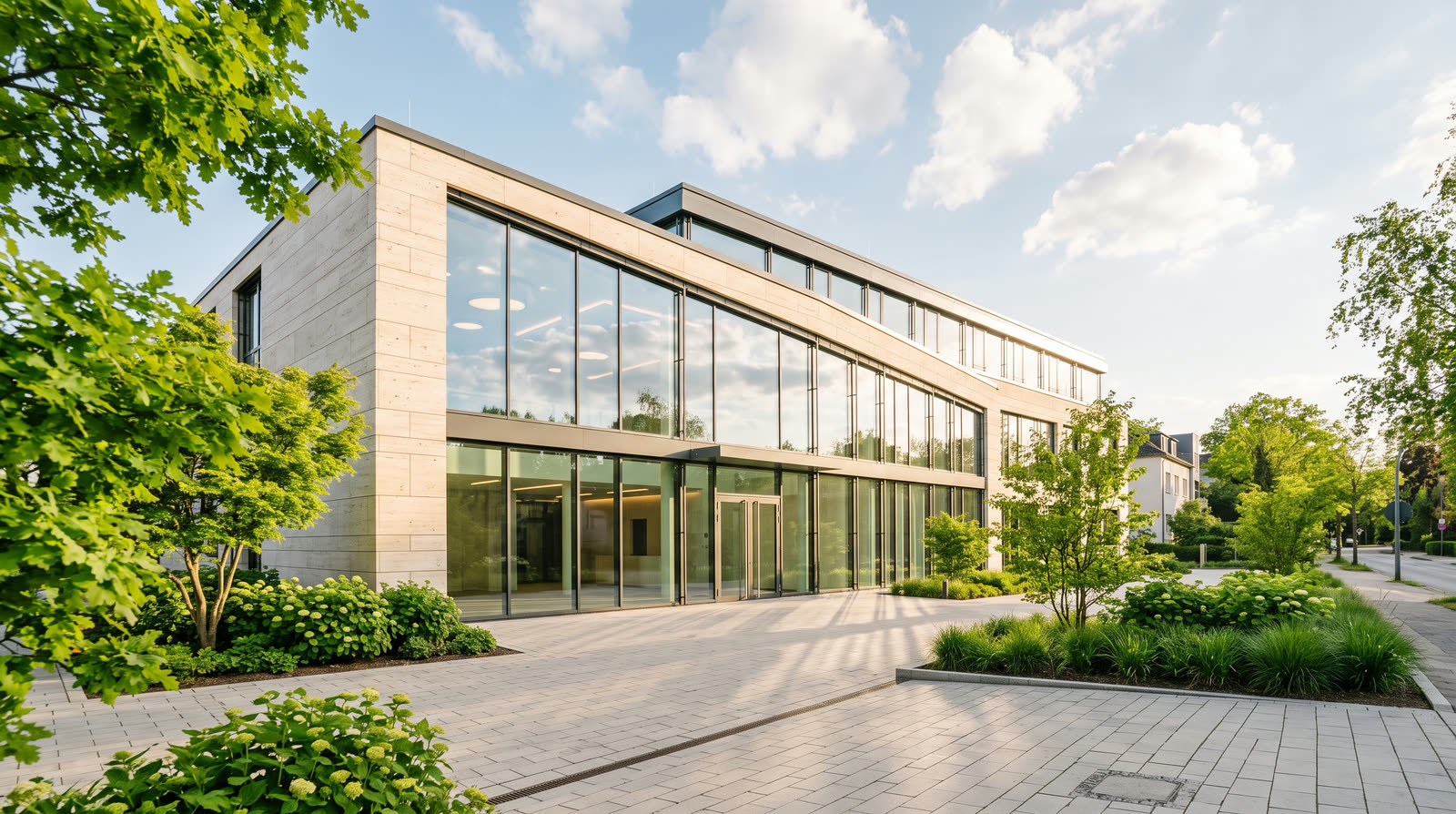 Modernes Bürogebäude bei Tageslicht mit Bäumen und gepflastertem Vorplatz